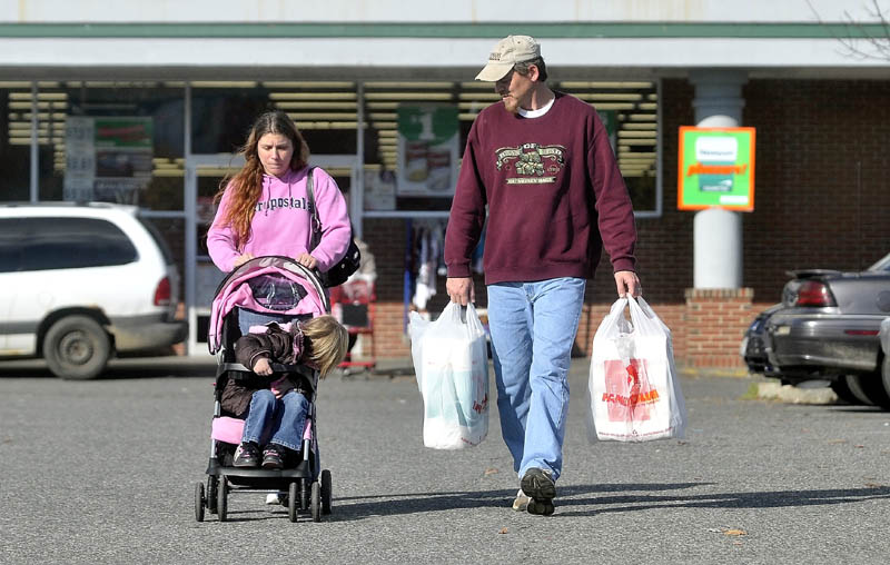 Janet White pushes her daughter, Savannah LaBrie, in a stroller as Jeff White carries groceries, after shopping at Family Dollar in Waterville on Nov. 2. Their car was also destroyed in the same fire that burnt their Waterville home, leaving the family to rely on friends and family to get around town. On this day they couldn't find a ride and had to walk the two miles from home to the store.