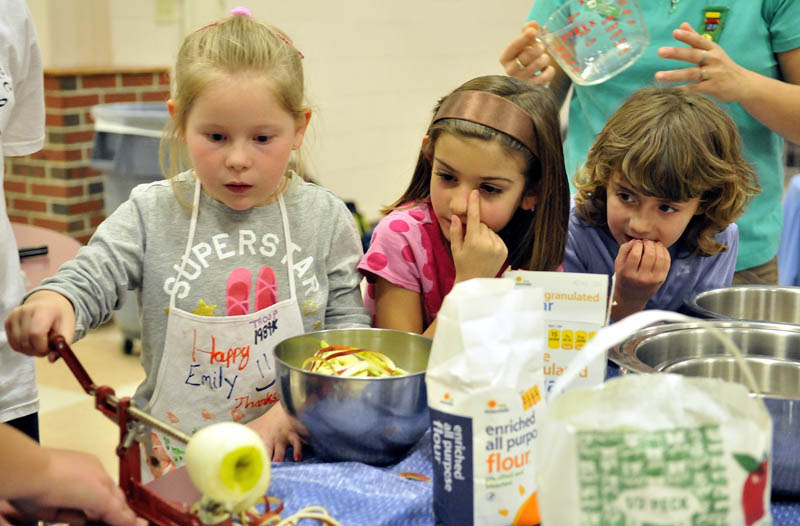 Hannah Robertson, 6, right, and Lynzi Trepanier, 6, center, watch as Abbigail Kolreg, 6, left, peels an apple with a mechanical peeler as the girls prepare apple pies in the cafeteria at Messalonskee High School on Tuesday. Girl Scout Troop 1989 has been preparing pies for the community Thanksgiving dinner at Messalonskee High School since 1997.