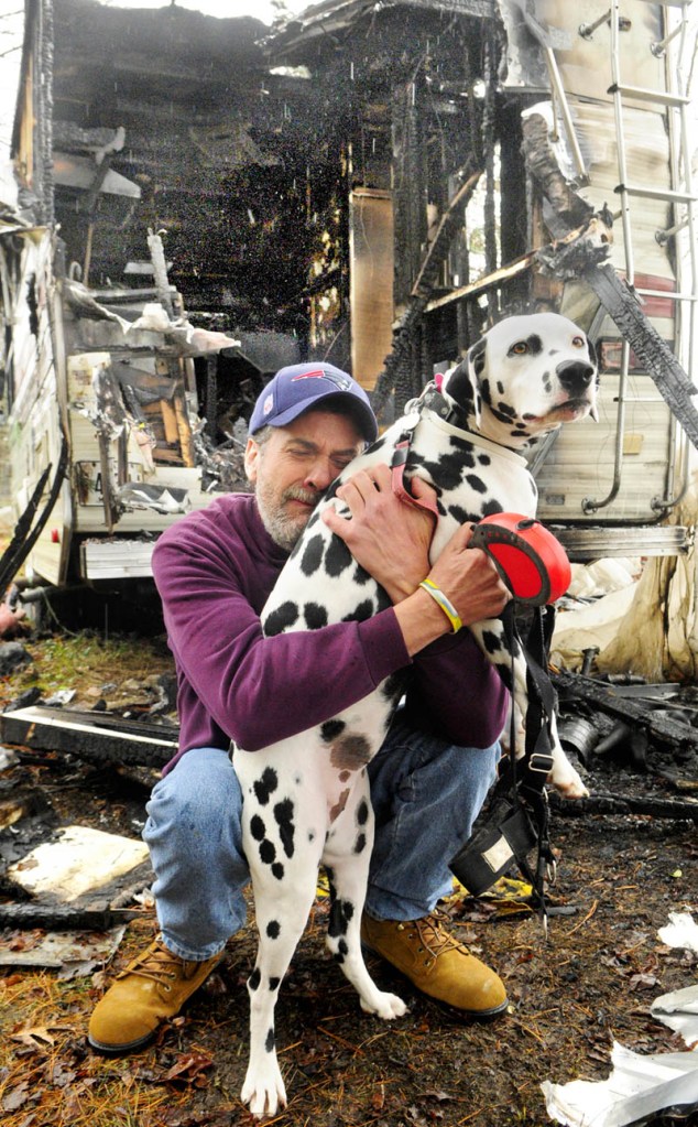 Robert Wing kneels with his Dalmatian, Brie, held tightly in front of their charred motor home on Tuesday afternoon in Augusta.