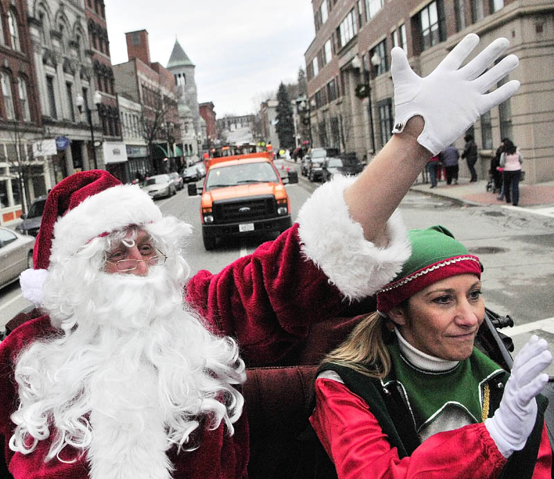 Santa Claus, left, and Jingle the elf wave as they ride down Water Street in a horse-drawn carriage, driven by Cathy Simmons of S&S Carriage Rides, before the annual tree lighting events on Saturday, on Water Street in downtown Augusta.