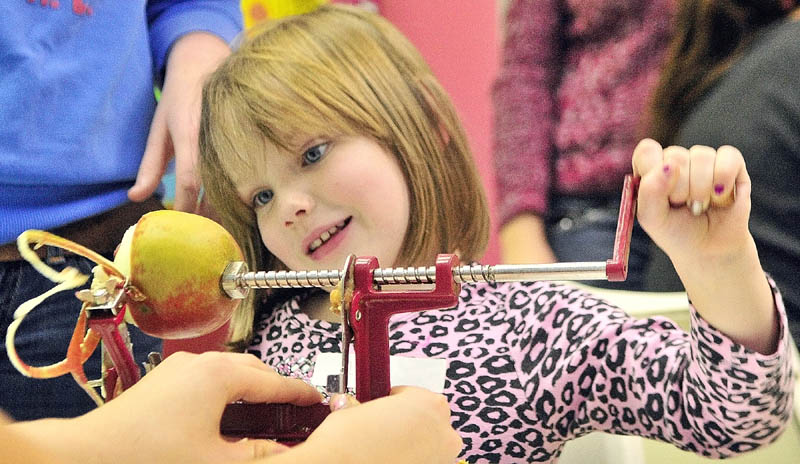 Lauren Miller, 5 of Winthrop, cranks an apple peeler-slicer on Wednesday afternoon at the Children's Discovery Museum in Augusta. She and other children made a crust, prepared apples and covered it all with a crumb topping during the museum's annual Make, Take and Bake event.