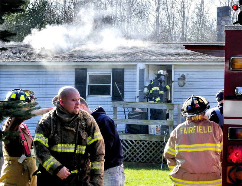 Smoke pours out through the roof of a mobile home badly damaged by fire on the Martin Stream Road in Fairfield on Monday, as firefighters change air tanks and enter the home.