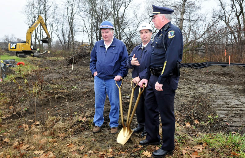 As workers remove trees in background, Waterville City Manager Michael Roy, center, motions to Police Chief Joseph Massey during a groundbreaking ceremony at the site of the new police department at Colby Circle on Tuesday. At left is City Councilor Fred Stubbert.