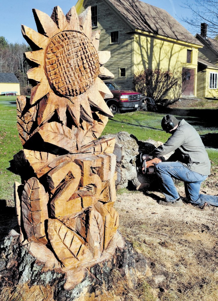 Eric Ogden cuts up sections of a maple tree left over after sculptor Pasco Grove carved the trunk into a large sunflower and street number at Ogden's home in Winslow on Sunday.