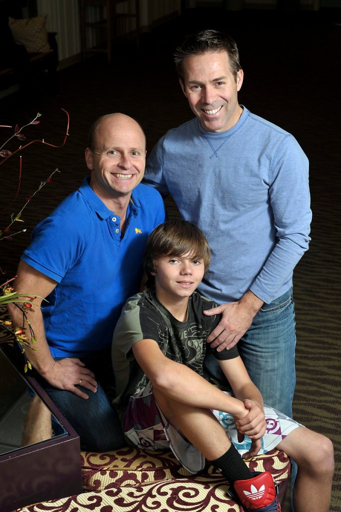 Ray Dumont, left, partner Rodney Mondor, right, and their son, Ethan Mondor, pose for a family portrait at Lyric Theater in South Portland. The men got engaged at Tuesday’s Question 1 victory celebration.