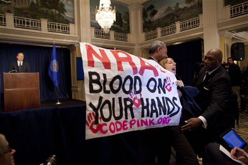 Activist Medea Benjamin, of Code Pink, is led away by security as she protests during a statement by National Rifle Association executive vice president Wayne LaPierre, left, during a news conference in response in Washington on Friday.