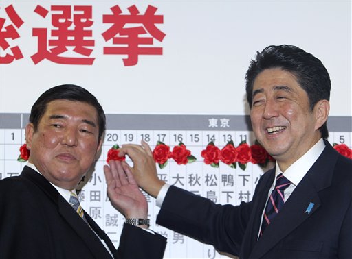Japan's main opposition leader Shinzo Abe, right, of the Liberal Democratic Party, and the party secretary-general, Shigeru Ishiba, place a rosette on the name of one of those elected in parliamentary elections at the party headquarters in Tokyo on Sunday. The conservative LDP stormed back to power Sunday after three years in opposition, exit polls showed.