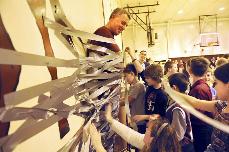 Monmouth Middle School principal Steve Philbrook is taped to a wall in the gym on Monday, during a schoolwide assembly of students and faculty. The students were promised a chance to tape the principal to the wall if they assembled more food items than last year for the annual Cottrell-Taylor food drive. Students from the 4th through 8th grades surpassed last year's collection by gathering 3,454 nonperishable items to donate during the holidays to several area families. After a several rolls of tape were applied, a box beneath Philbrook's feet was removed, and he remained firmly in place until faculty cut him loose.