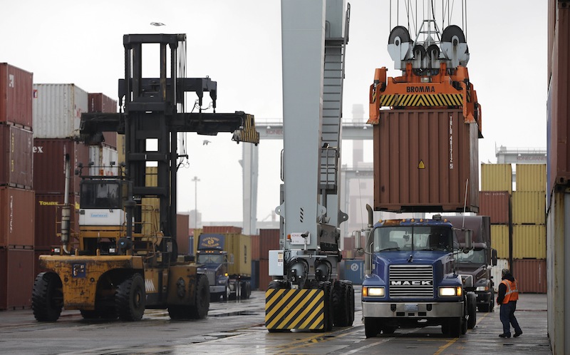 A truck driver watches as a container crane lowers a freight container onto a tractor trailer at the Port of Boston. The crane and a reach stacker, left, are operated by longshoremen at the port. The longshoremen's union has agreed to extend its contract until Feb. 6.