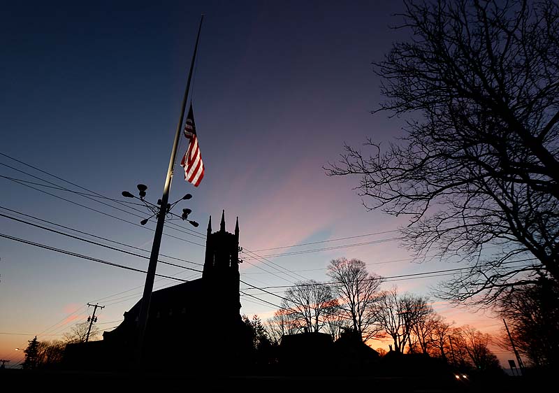 A U.S. flag flies at half-staff as vehicles drive on Main Street in downtown Newtown, Conn., as the sun rises Saturday morning after a gunman opened fire inside a nearby elementary school.