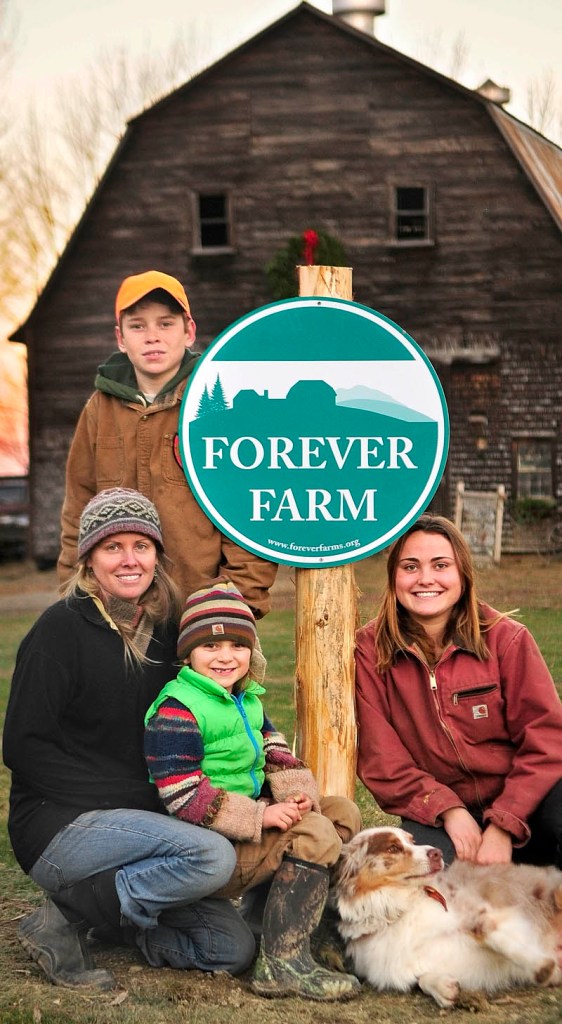 Mary Perry, left, and her children Gil Whitehead, standing, Sage Whitehead, seated on lap, and Kenya Whitehead, pose beside the Forever Farm sign at their Winterberry Farm, on Thursday in Belgrade.