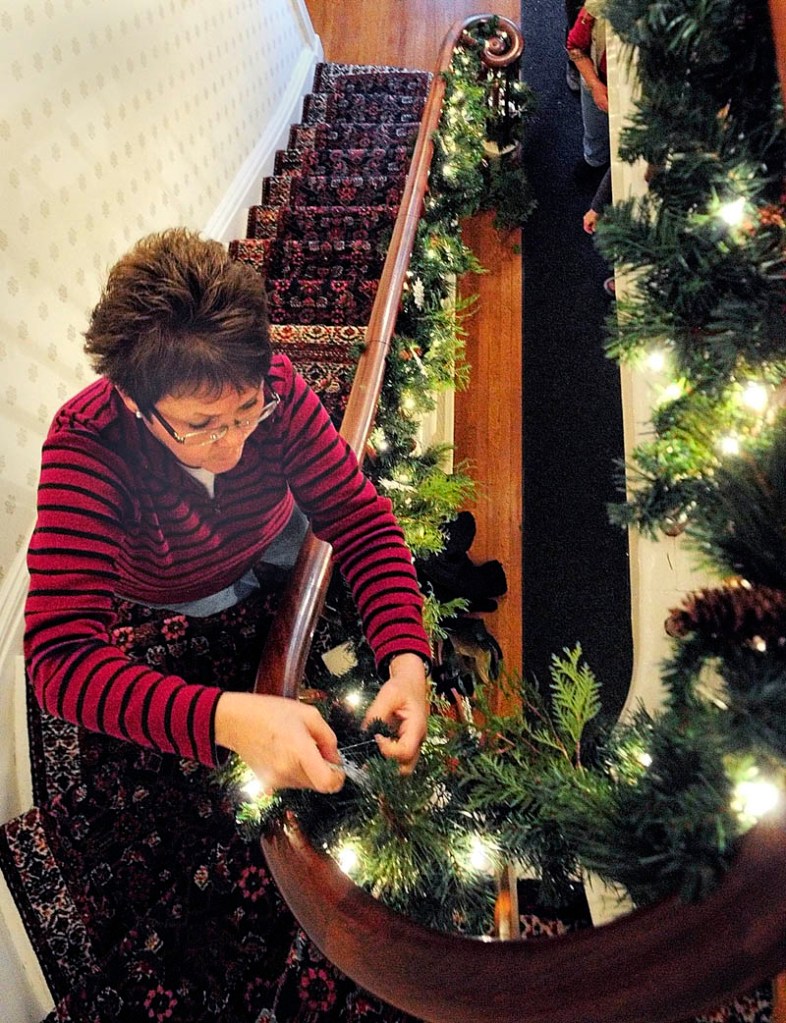 Shelly Hanson, of Chelsea, attaches a snowflake to the garland hanging off the front entryway banister on Tuesday at the Blaine House, in Augusta.
