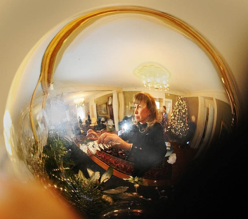 Maggie Kelley is reflected in a large silver ball as she decorates a fireplace mantle on Tuesday at the Blaine House in Augusta.
