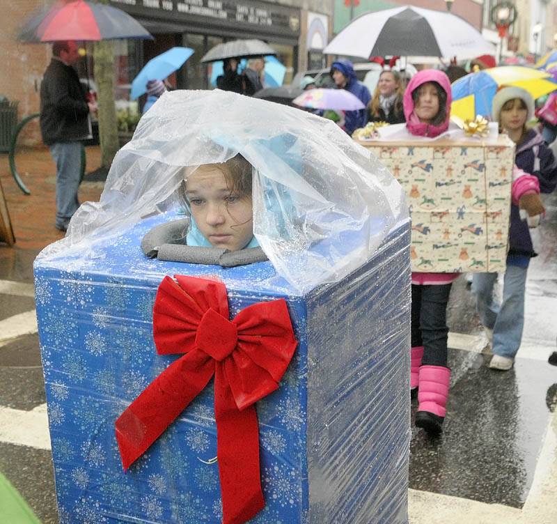 Thekla Jubinville wears a rain poncho over her wrapped present costume, as she marches down Water Street in the "Who's Your Favorite Who" parade on Saturday, in downtown Gardiner. Despite the rain the parade went on and Santa and Mrs. Claus arrived in a horse drawn wagon.