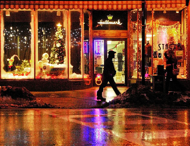 People walk past the brightly decorated windows of Stacy's Hallmark on Water Street in downtown Augusta on Tuesday.