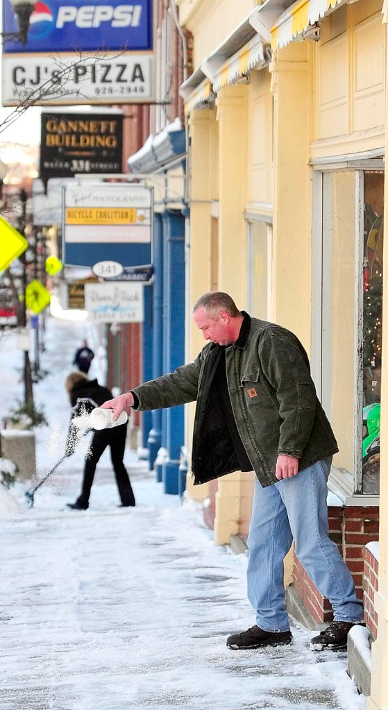 Augusta Pawn and Jewelry employee Troy Hanscom spreads salt in front of the store on Friday on Water Street in downtown Augusta. Building owner Karen Hatch shovels snow further up the street.