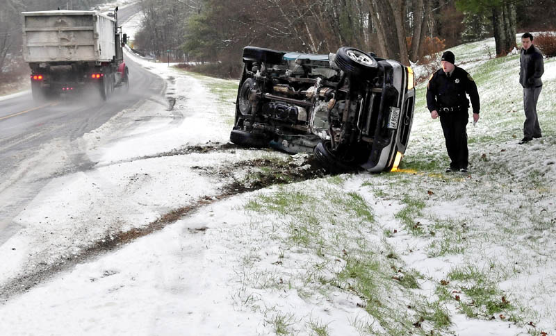 Kennebec County Sheriff's Office Deputy Jacob Pierce investigates a truck rollover, after the vehicle left ice and slush-covered Route 139 in Benton, on Monday. The uninjured driver is at right. Pierce said the slippery road condtions are to blame for the accident.