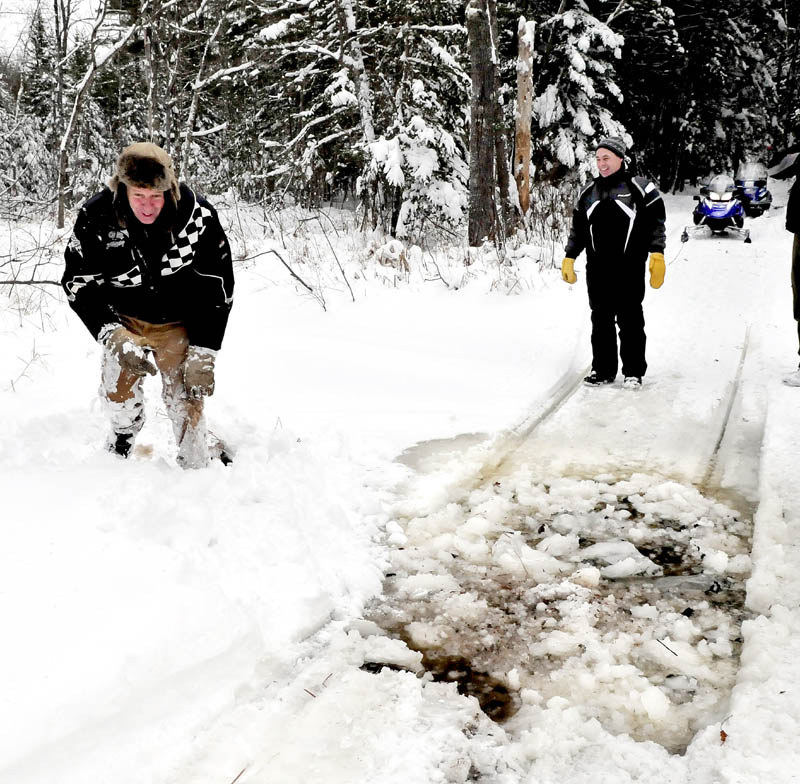 Belgrade Draggin Masters club member Ernie Rice, left, gets up after breaking through ice in a shallow stream along a snowmobile trail in Belgrade on Sunday. Dennis Harris waits to cross with his groomer.