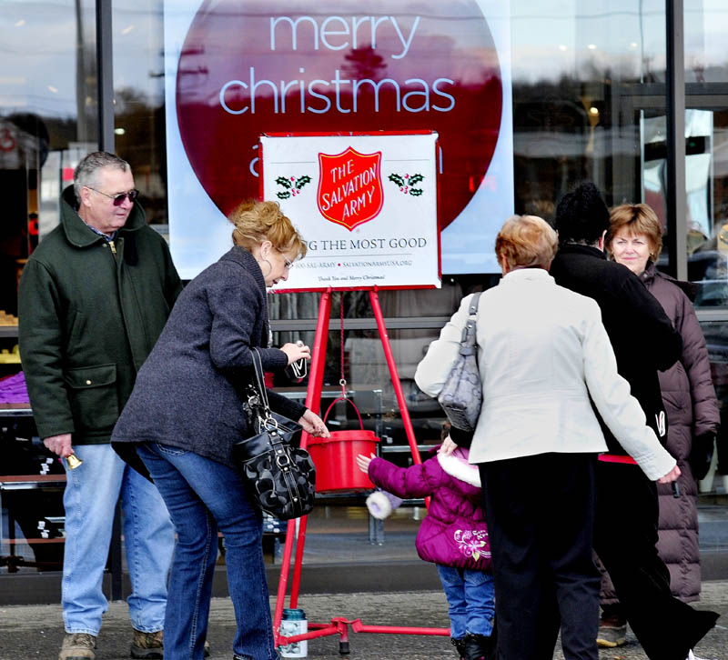 Salvation Army bellringers Gary Mullins and his wife, Jean, at right, greet shoppers as Carol Noel helps her grandaughter, Peyton, drop money in the kettle at Elm Plaza in Waterville on Monday. "People have been very generous," Gary Mullins said.