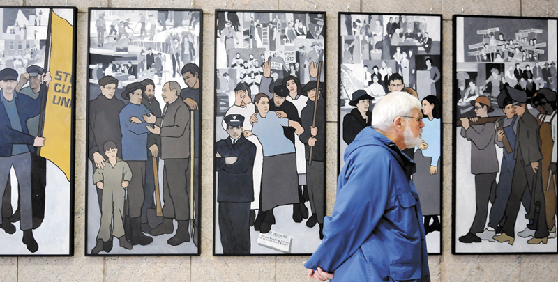 Ken Jones, of Farmingdale, examines the labor murals that are now hanging on the wall of the Cultural Building atrium that serves as the entryway to the Maine State Museum in Augusta Monday. The murals were hung over the weekend after being removed by Gov. Paul LePage in 2011 from the Department of Labor.