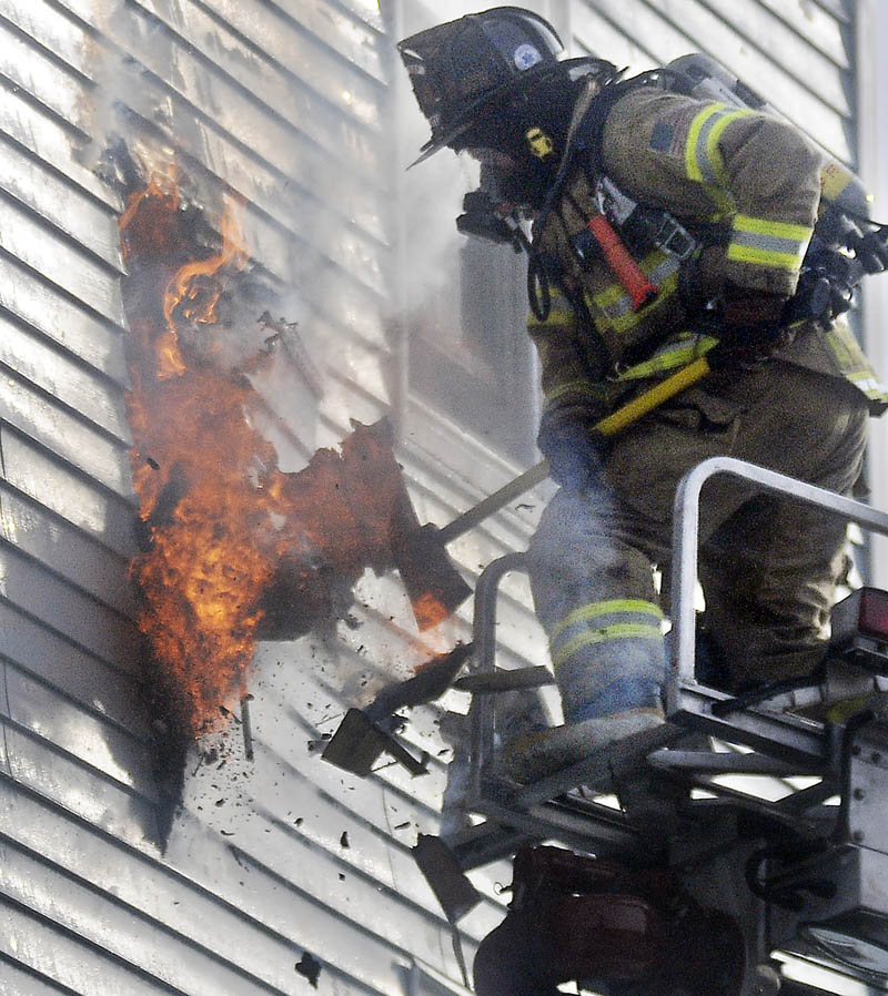 A firefighter exposes an exterior wall Tuesday at 1 Penobscot St. in Augusta. Fire heavily damaged the apartment building.