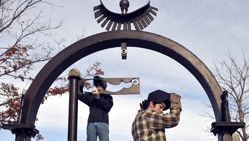 Aaron Dufour, left, replaces the top of a piece of the sculpture that he helped install Sunday with Ben Stoodley, right, and other classmates from the University of Maine at Augusta, at the Viles Arboretum in Augusta.