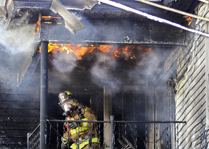 An Augusta firefighter ducks beneath flames emerging from the third-floor deck of an apartment building that burned Thursday on Sewall Street.