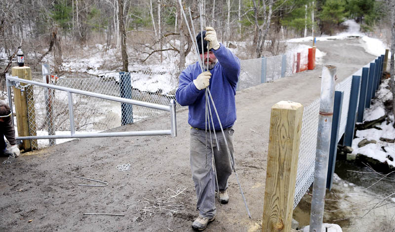 Cobey Schmidt picks up pieces of fencing that he helped erect Tuesday with his colleague, Greg Roy, on the bridge spanning Bond Brook at the Bond Brook Recreation Area in Augusta. The employees of Androscoggin Fence Company were putting up rails and gates on the trailhead for bikers and runners.