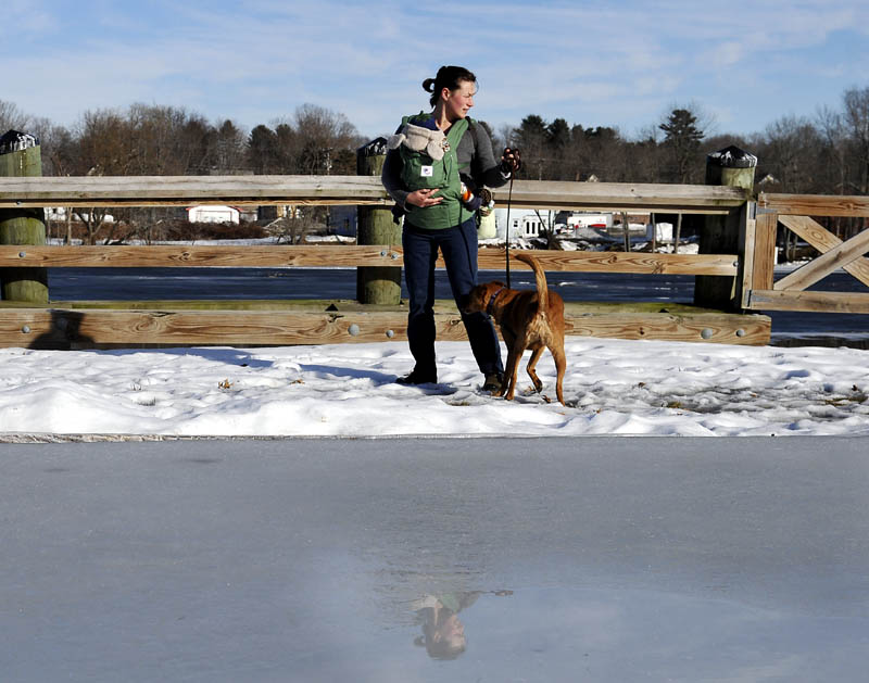 Nettie Pangallo, of Richmond, leads her dog past the ice rink at the Gardiner waterfront on the Kennebec River on Monday, while taking her infant son, Atticus, for a walk in temperatures in the mid-50s F. Temperatures are forecast to drop later this week.