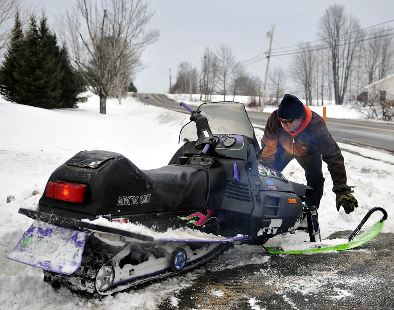 Larry Murphy moves a snowmobile off a patch of tar in a driveway Wednesday while commuting home from his job in Augusta. Murphy said he hit a soft patch of snow, forcing him to detour across the driveway.