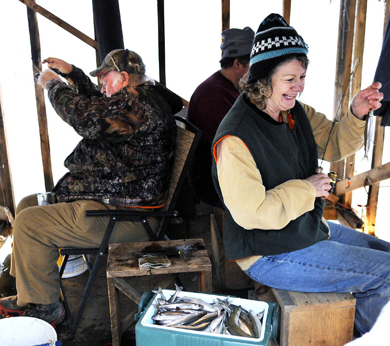 Grace Peters, right, unhooks a smelt Sunday while fishing with Roger Cahoon, center, and Jim Earle Sr. at Baker's Smelt Camps. The winter angling shacks, rented by the tide, have emerged from Merrymeeting Bay to Randolph on the Kennebec River. The migrating fish are "really running now," Baker's Smelt Camps owner Mike Baker said.