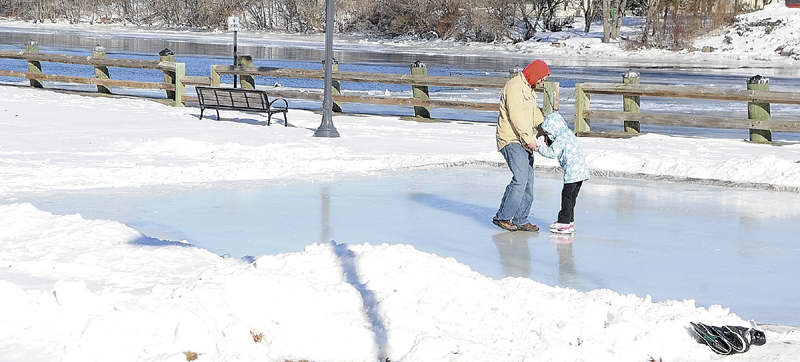 Manuel Manos, left, teaches Lily Matos to ice skate Saturday at the new rink beside the Kennebec River in Gardiner's Waterfront Park.