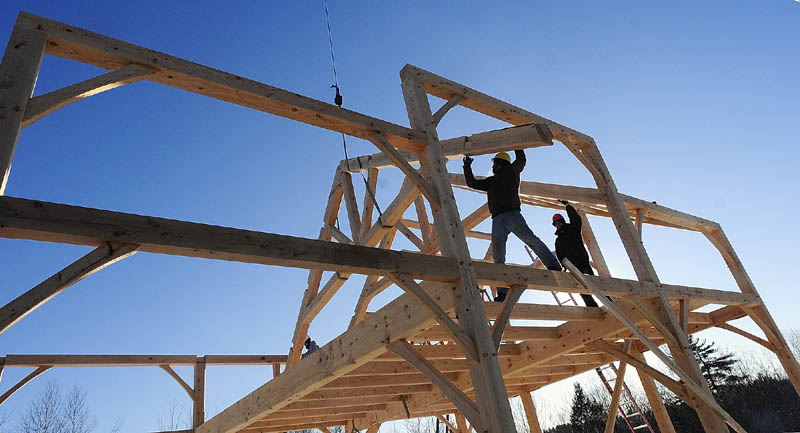 Workers lower a roof truss into position on Friday at the Grand View Timber Frames display site on Western Avenue in Manchester.