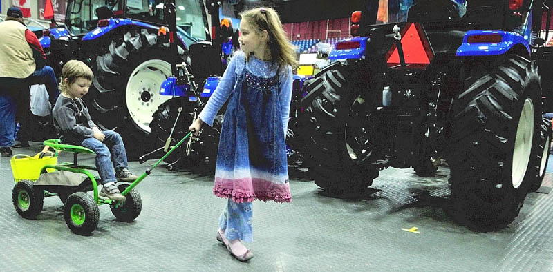 Oliver Kucharski, 3, left, gets a ride from his sister, Maya Kucharski, 8, both of Sidney, past some tractors at the Maine Agricultural Trades Show on Thursday at the Augusta Civic Center.