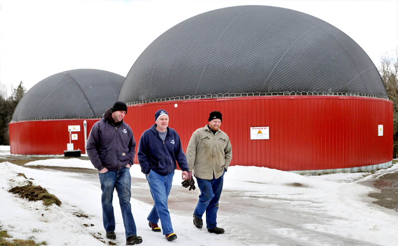 Adam Wintle, left, Travis Fogler and John Wintle walk past the two digester buildings, where food waste and cow manure are mixed to produce gas that powers a generator for electricity, at Stonyvale Farm in Exeter.