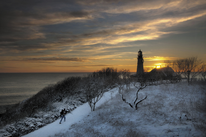 Clearing skies await a tripod-toting photographer looking for a spot to capture the early-morning light at Portland Head Light Thursday, in Cape Elizabeth. A snowstorm that ended before dawn temporarily transformed Fort Williams Park into a snowy scene.