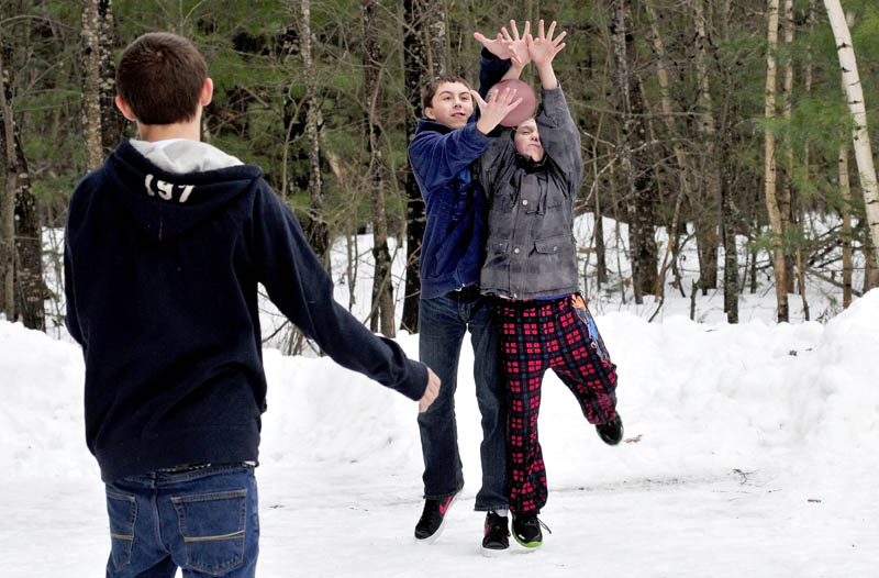 Caleb Latham, left, watches as Tylor Latham, center, and Deven Boyker reach for a football, in Farmington on Sunday. The mild temperatures melted snow and ice and allowed the boys to have a game of catch.
