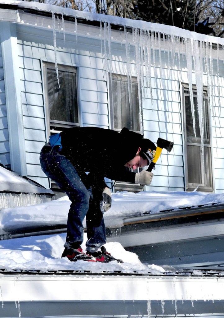 Josh Mosher uses an axe to break up ice that froze on a roof at his home on Lincoln Street in Waterville on a chilly Wednesday.
