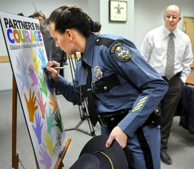 Maine State Police Lt. Anna Love signs the board for the Children's Advocacy Center with Kennebec County Sheriff's Det. Sgt. Frank Hatch, right, Monday during a ceremony in Augusta to the mark the center's new interagency agreement to provide sexually abused children streamlined access to investigators and social services in Kennebec and Somerset Counties.