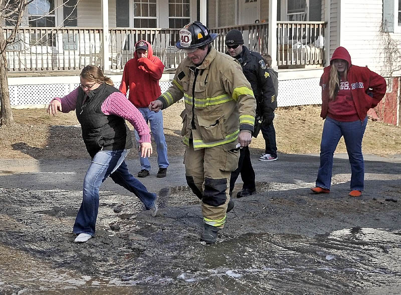 Kimberly Guite, 46, left, leaps over a pool of water in her socks with the help of Waterville Fire department Lt. Scott Holst, on Squire Street in Waterville Thursday. Guite lost her rental home to fire. Guite narrowly escaped a fire that broke out in her home. She didn't have time to put her shoes on.