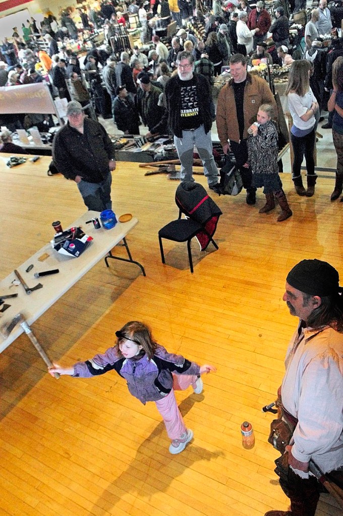 Molly Turnbull, 7 of Knox, left, tosses a tomahawk at the target, after getting instructions from David "Gomer" Bryant, right, during the Ancient Ones of Maine Sport and Gun Show on Saturday at the Augusta Armory. Bryant, of Mount Vernon, said that he's been doing the throwing demonstrations for more than 20 years.