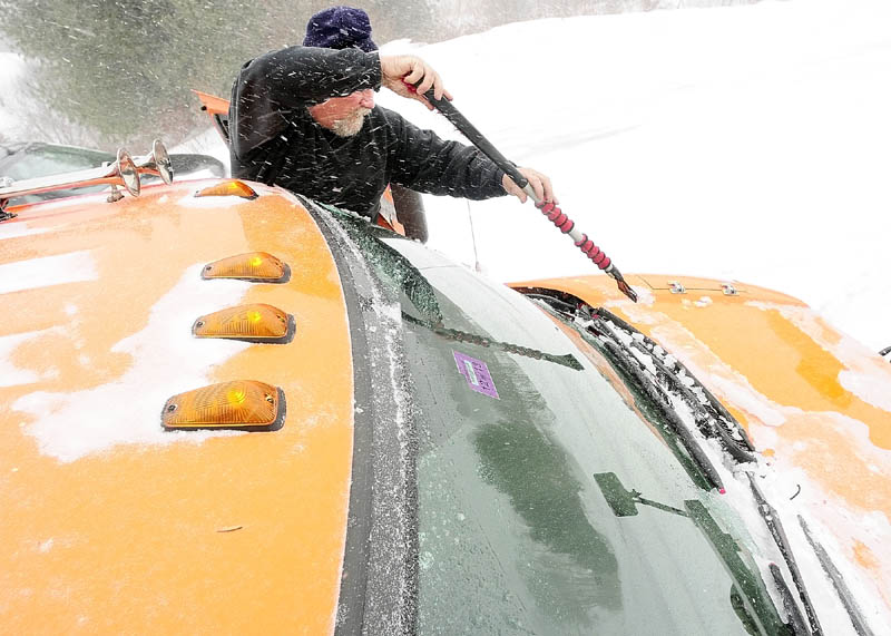 Augusta Public Works plow truck driver Stan Moore scrapes ice off the windshield while plowing rural roads on Saturday.
