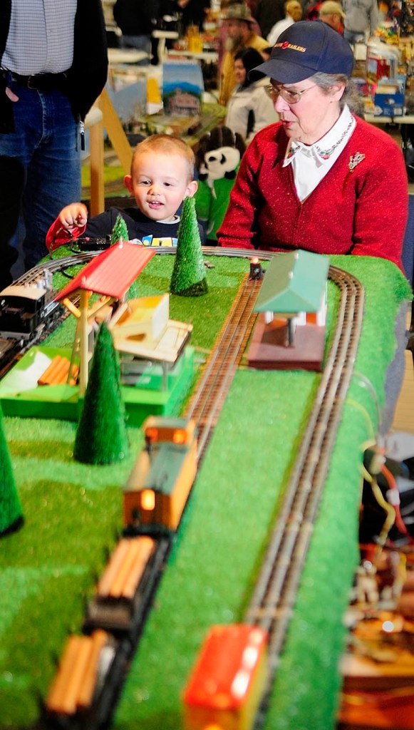Connor Ruttenberg, 2 1/2, of Turner, pushes the buttion to unload logs from a model train with some help from Joanne Burns, of Friendship, at the Maine 3-Railers display on Saturday, during the Whitefield Lions Club Model Railroad & Doll House Show at the Augusta armory.
