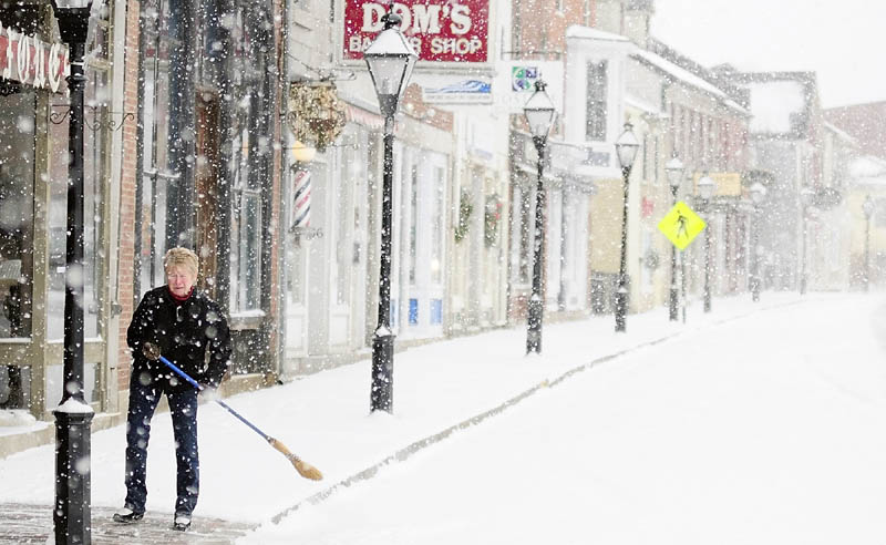 Linda Lesieur sweeps snow off the sidewalk this morning in front of the Earthbound shop on Water Street in downtown Hallowell
