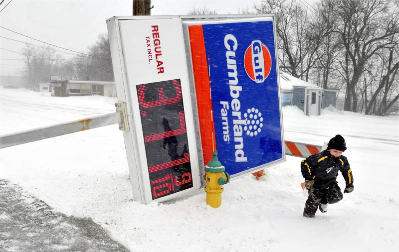 Liam Poulin runs back to his father's plowtruck after looking at the fallen sign at Cumberland Farms in Waterville. A store worker said the sign fell to the ground during strong winds before dawn on Saturday.
