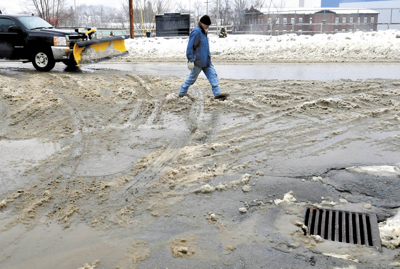 Don Holmes searches for dry ground while crossing a slush-covered street in Anson on Thursday. Warm temperatures turned a predicted snowstorm into a rainstorm yesterday.