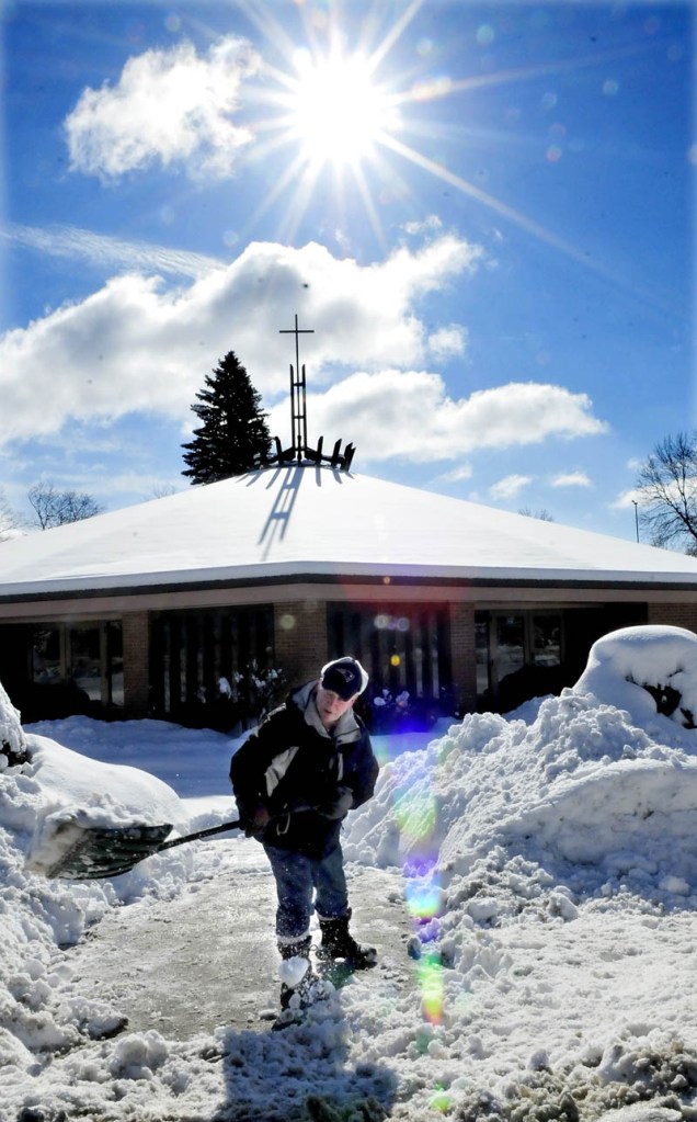 BLESS THIS MESS: Reggie Vashon shovels snow in the shadow of the sun and cross on the roof of Notre Dame Catholic Church in Waterville on Monday, Feb. 25, 2013.