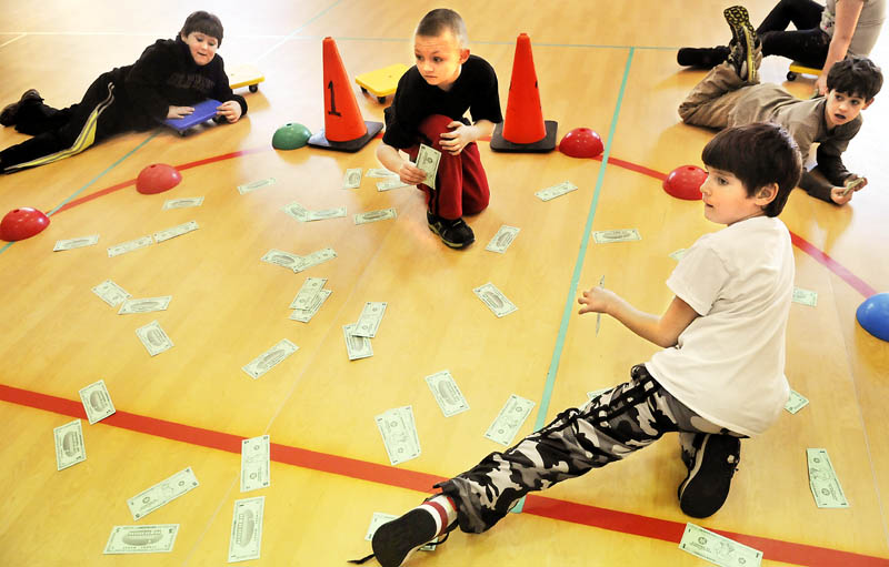 Whitefield Elementary School students roll across the floor of the gym on carts Tuesday, after collecting paper money to practice counting during physical education class.
