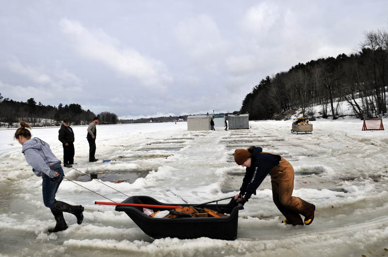 Airyn Jewett, left, and Kate Baker, both 14, haul a sled full of wood blocks they chiseled out of the Kennebec River Sunday, while removing shacks at Baker's Smelt Camps in Pittston. Friends, neighbors and employees helped proprietor Mike Baker remove the fishing shacks, rented to anglers by the tide, after the ice became brittle over the weekend. The wood that balanced the shacks over race holes for the winter.