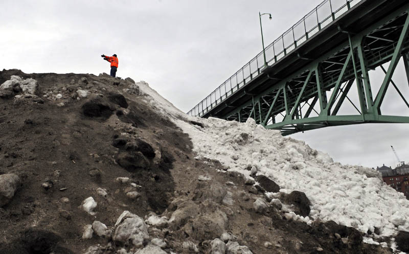Augusta Public Works employee Matt Jackson directs a truck to pour snow Thursday on the winter dump located on the banks of the Kennebec River, on the east side of Augusta. Workers were collecting snow from city schools and relocating it to the hill that rises to a height just below the catwalk underneath Memorial Bridge. The hill isn't as high as it has been in past winters, workers said, and usually melts by the end of spring.